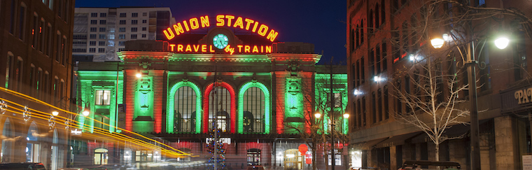 View of Union Station in downtown Denver, Colorado, taken at night from the middle of a street. The train station is lit up for the Christmas Holiday season